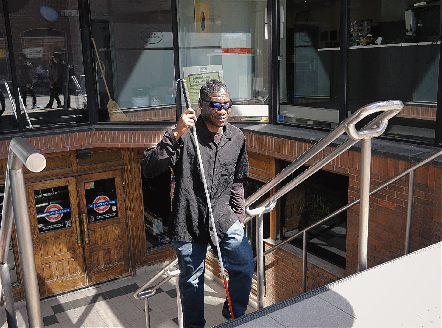 Ben Akuoko is walking up a set of stairs on a sunny day. The sunlight casts a gentle glow, highlighting his determined stride as he ascends. He wears a confident expression, his cane in hand, helping him navigate as he approaches the top. The bright and clear day, combined with Ben's focus, creates a scene of positivity, strength, and perseverance